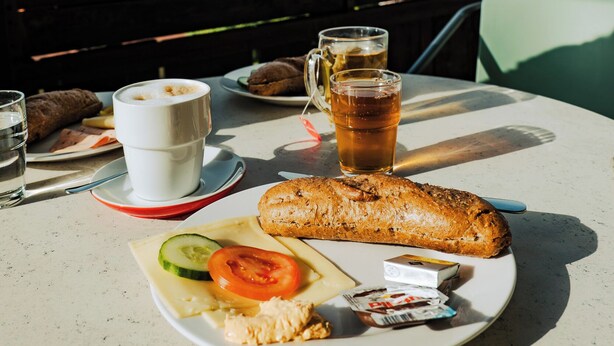 A table with a plate of food, a cup of coffee, and a glass of tea, set against a scenic mountain backdrop. - Mountain Hostel (Ramsau am Dachstein)