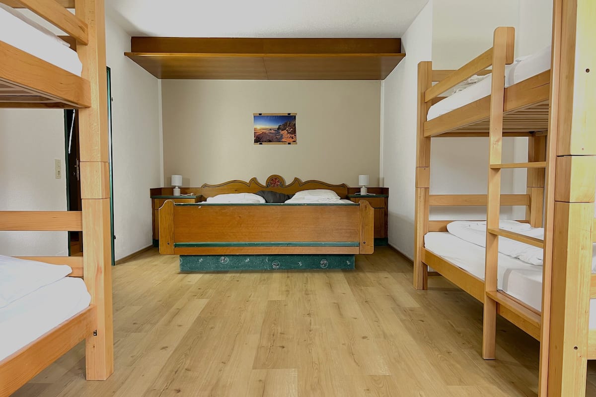 A room with a wooden bunk bed, a single bed, and a small bedside table with a lamp.