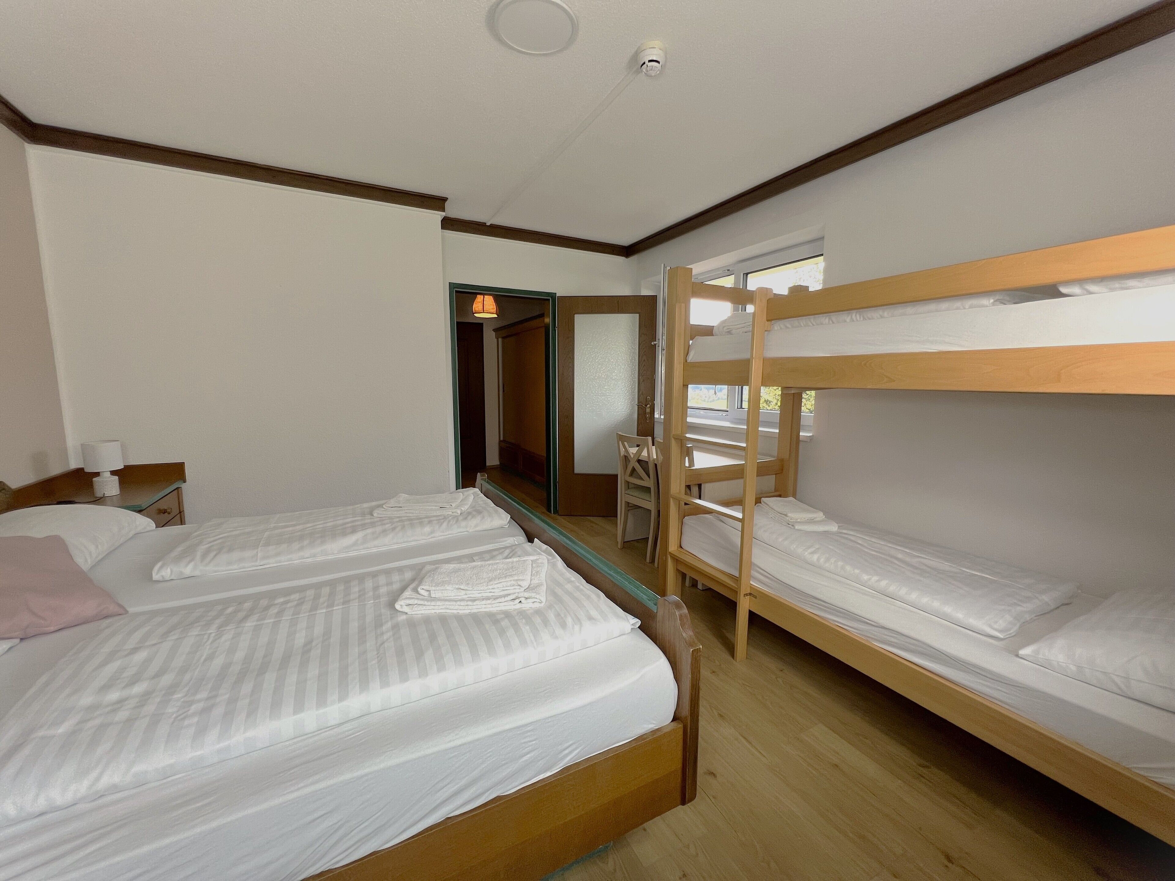 A room with two single beds, a wooden bunk bed, a desk with a chair, and a mirror.