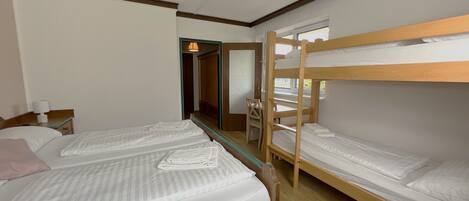 A room with two single beds, a wooden bunk bed, a desk with a chair, and a mirror.