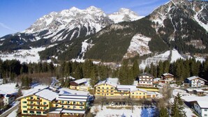 A mountain resort with multiple yellow buildings, a small lake, and snow-covered peaks in the background. - Mountain Hostel (Ramsau am Dachstein)