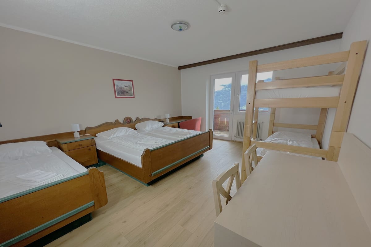 A bedroom with two wooden beds, a desk, and a chair. There is a window with a view of the outdoors.