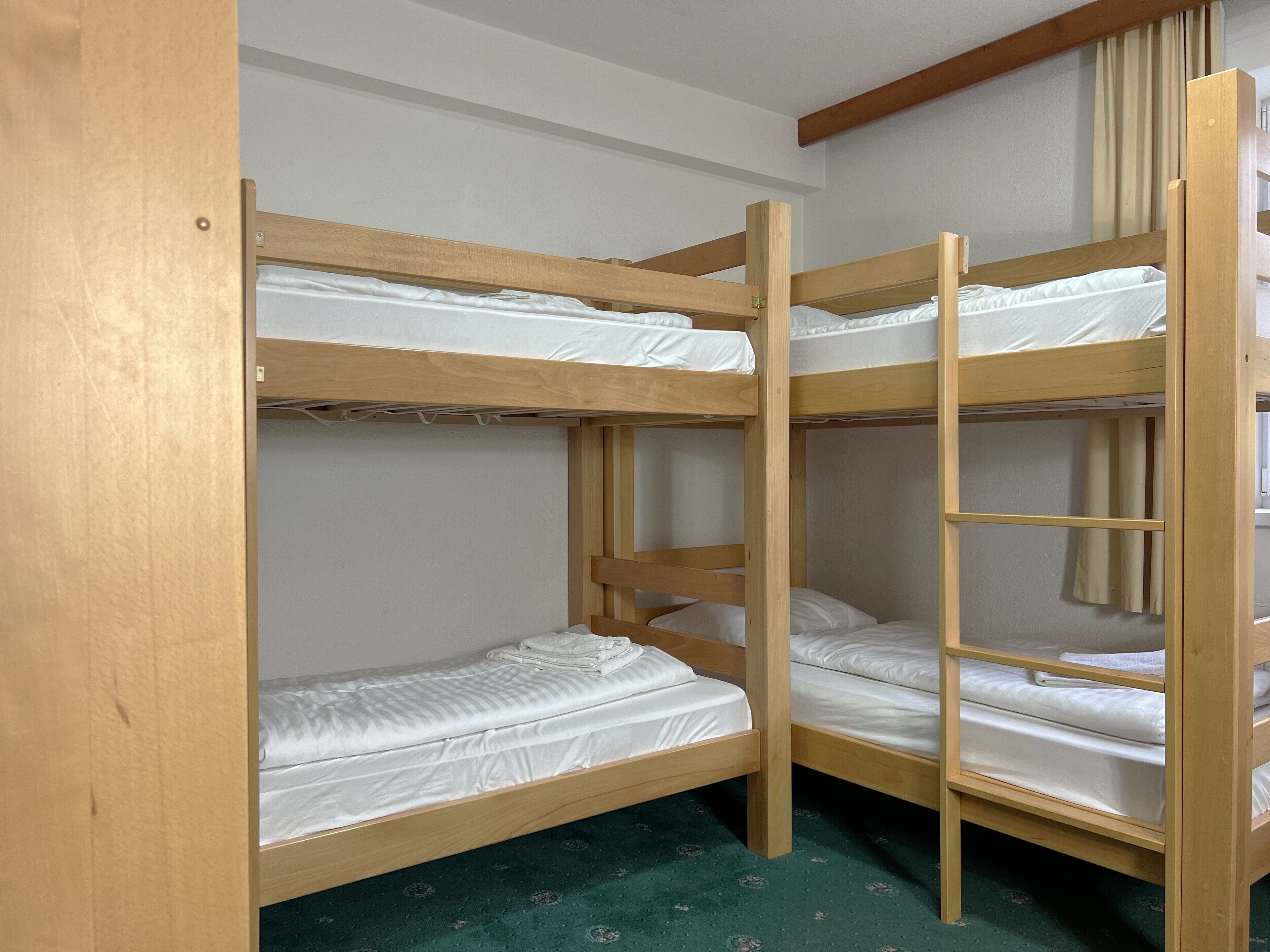 Ein Schlafraum mit Etagenbett, Holzrahmen, weißer Bettwäsche und einem grünen Teppich.