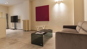 A modern living room with a glass coffee table, a red accent wall, a beige sofa, and a flat-screen TV. - Cozy studio apartment in the center of Bari, renovated and tastefully furnished (Bari)