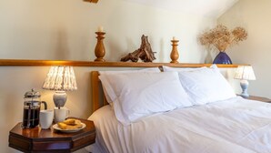 A neatly made bed with white linens, a wooden nightstand with a coffee pot, cups, and pastries, and a shelf with decorative items and candles. - Buckstone House Coach House, Forest of Dean - sleeps 4 guests in 2 bedrooms (Forest of Dean)