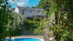 A pool surrounded by lush greenery, a white house with multiple windows, and a stone wall. - Buckstone House Coach House, Forest of Dean - sleeps 4 guests in 2 bedrooms (Forest of Dean)