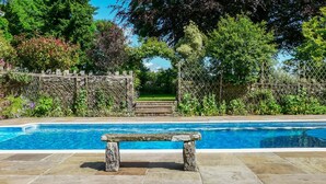 A swimming pool with stone benches, surrounded by lush greenery and a stone wall. - Buckstone House Coach House, Forest of Dean - sleeps 4 guests in 2 bedrooms (Forest of Dean)