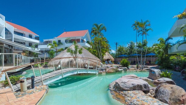 A resort with a swimming pool, thatched-roof structures, palm trees, and modern buildings. - Noosa International 145 Noosa Heads (Noosa Heads)