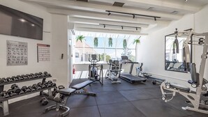 A modern gym with various exercise equipment, a bench, dumbbells, and a large window with plants. - Noosa International 145 Noosa Heads (Noosa Heads)