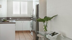 A modern kitchen with white cabinets, a stainless steel refrigerator, and a glass table with a plant. - Noosa International 145 Noosa Heads (Noosa Heads)