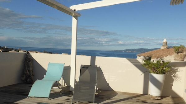 A terrace with two lounge chairs, a potted plant, and a view of the sea and distant buildings. - EXCELLENT APARTMENT WITH LARGE TERRACE AND OCEAN VIEW - 5-MINUTE WALK TO DOWNTOWN AND THE BEACH + PARKING SPACE (Propriano)