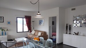 Una sala de estar moderna con una mesa de comedor de vidrio, sillas blancas, un sofá color beige y una cortina roja.