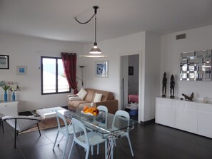 Ein modernes Wohnzimmer mit einem Glastisch, weißen Stühlen, einem beigen Sofa und einem roten Vorhang.