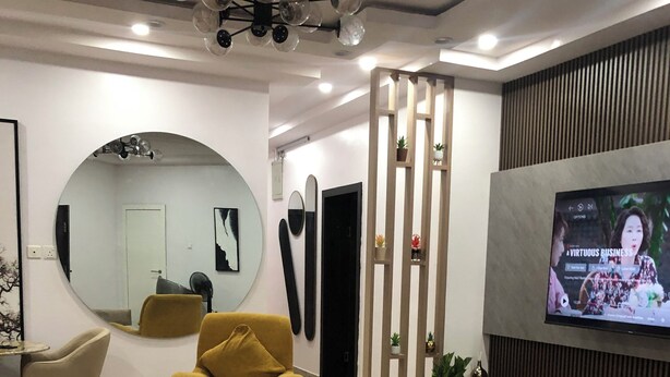 A modern living room with a sofa, armchair, and round coffee table. A television is mounted on the wall, and there is a mirror on the wall. - Spacious 3-bedroom apartment with AC, WiFi in fabulous Ikeja (Ikeja)