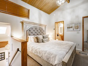 Een slaapkamer met een groot bed, een houten hoofdeinde en een spiegel aan de muur.