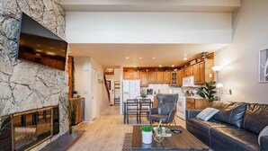 Een moderne woonkamer met een stenen openhaard, een leren bank en een eethoek met houten kasten.