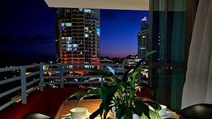 A dining area with a table set for two, a potted plant, and a view of the cityscape at dusk.