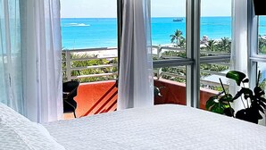 A hotel room with a large window offering a view of the ocean and a balcony with plants.
