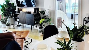A modern living room with a flat-screen TV, a dining table with chairs, and several potted plants. - Beach View at 101 Ocean Drive, SoFi in Miami Beach (Miami Beach)