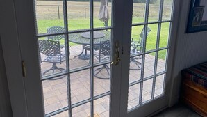 A view through a glass door to an outdoor patio area with a table and chairs, a lawn, and a fence. - Cozy 1-bedroom apartment in charming Burton 9 minutes from ROUND TOP! (Burton)