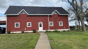 A red two-story building with a dark roof, a front door, and a small porch area. - Cozy 1-bedroom apartment in charming Burton 9 minutes from ROUND TOP! (Burton)