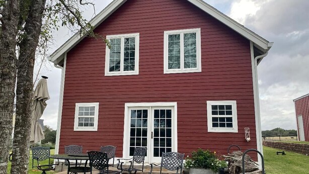 A red two-story house with a patio, a table, and four chairs. - Cozy 1-bedroom apartment in charming Burton 9 minutes from ROUND TOP! (Burton)