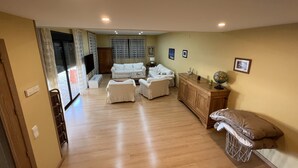 Un salon spacieux avec un plancher en bois, un ensemble de canapés blancs, un meuble en bois et un téléviseur.