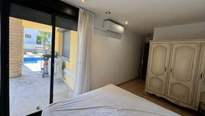 Une chambre avec un lit, une armoire et une porte-fenêtre coulissante donnant sur un balcon avec une piscine.