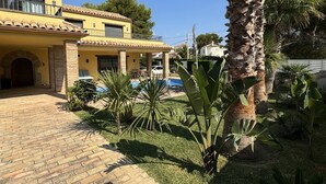 Une villa jaune avec un toit en tuiles, une piscine et un jardin bien entretenu agrémenté de palmiers.