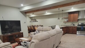 Una sala de estar con un televisor de pantalla plana grande, sofás color beige, un comedor con sillas de madera y una cocina con gabinetes de madera y electrodomésticos de acero inoxidable.