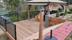 Una terraza de madera con un pabellón, una silla y una zona de barbacoa con vistas a un río.
