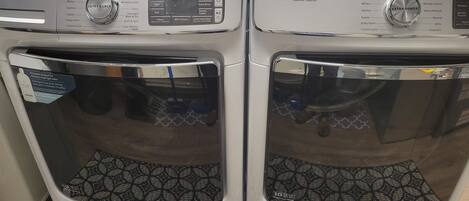Two Maytag front-loading washing machines with control panels, a small table with cleaning supplies, and a patterned rug on the floor.