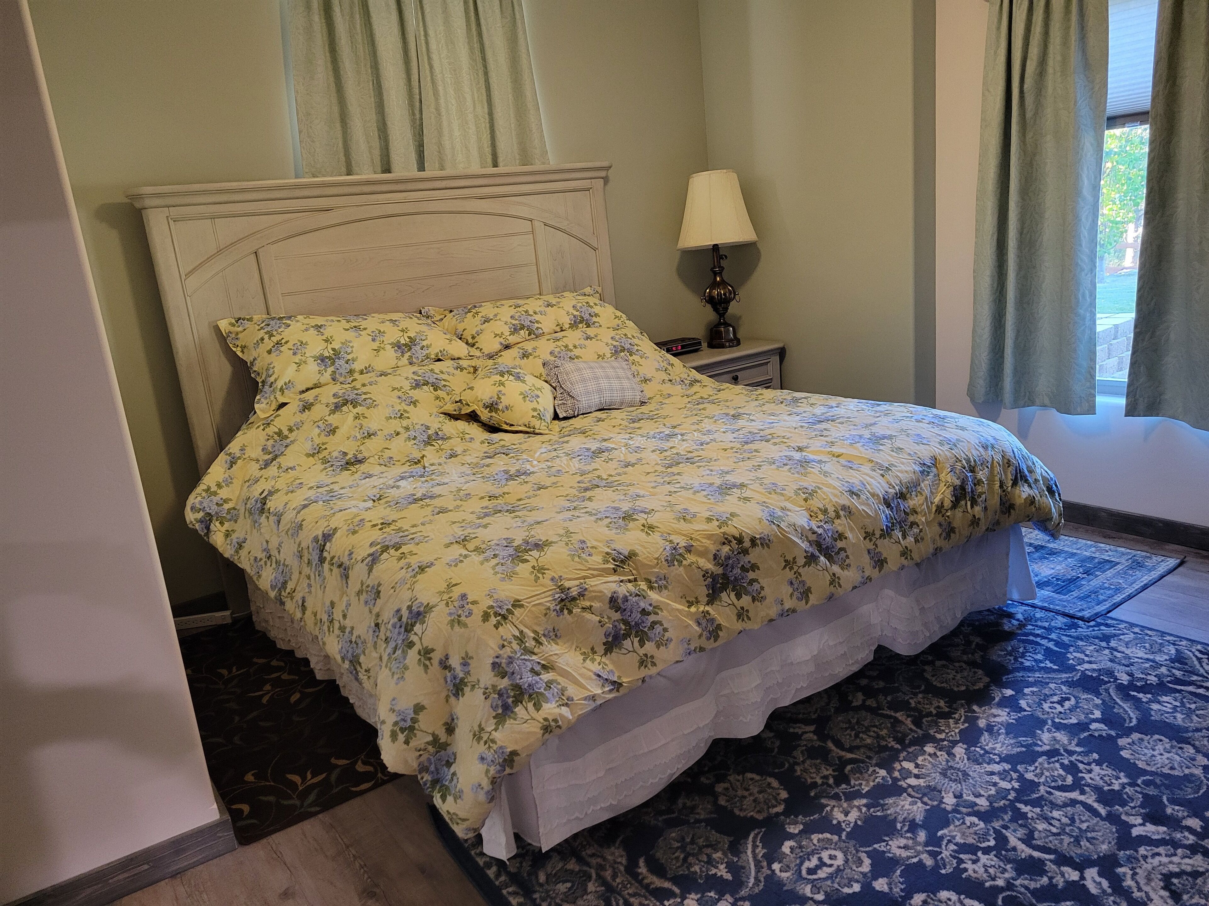 A bed with floral bedding, a bedside table with a lamp, and a patterned rug.