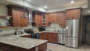 Una cocina moderna con armarios de madera, electrodomésticos de acero inoxidable, encimeras de granito y una zona de bar con taburetes.
