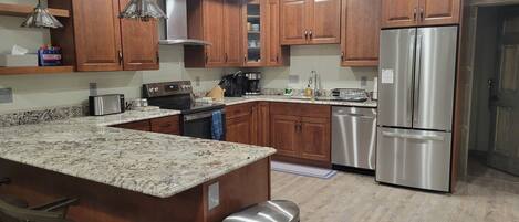 A modern kitchen with wooden cabinets, stainless steel appliances, granite countertops, and a bar area with stools.