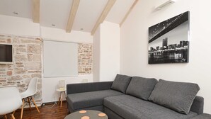 A modern living room with a grey sectional sofa, a round coffee table with orange accents, a white chair, and a cityscape painting on the wall. - Trendy and Chic Rovinj Downtown Apartments (Rovinj)