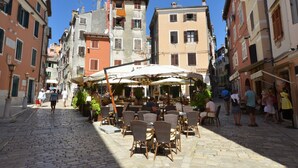A cobblestone street lined with historic buildings, outdoor seating at a café, and a clear blue sky. - Trendy and Chic Rovinj Downtown Apartments (Rovinj)