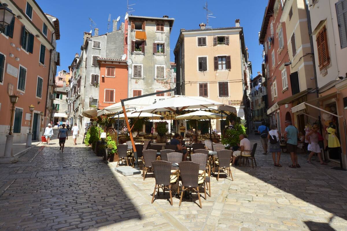 A cobblestone street lined with historic buildings, outdoor seating at a café, and a clear blue sky.