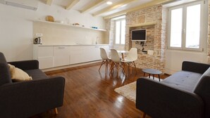 A modern living room with a kitchen area, wooden flooring, and a stone wall. - Trendy and Chic Rovinj Downtown Apartments (Rovinj)