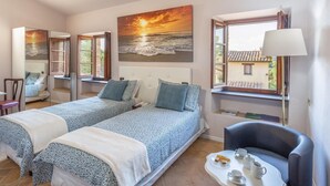 A bedroom with two beds, a chair, a table with cups and pastries, and a painting of a sunset over the sea. - Agriturismo Borgo Pulciano in Montone (Montone)
