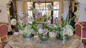 Una mesa redonda de mármol con centros de mesa florales en un vestíbulo con columnas ornamentadas y suelo estampado.