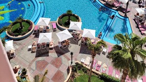 Zona de piscina en un complejo turístico, con varias piscinas, tumbonas y palmeras.