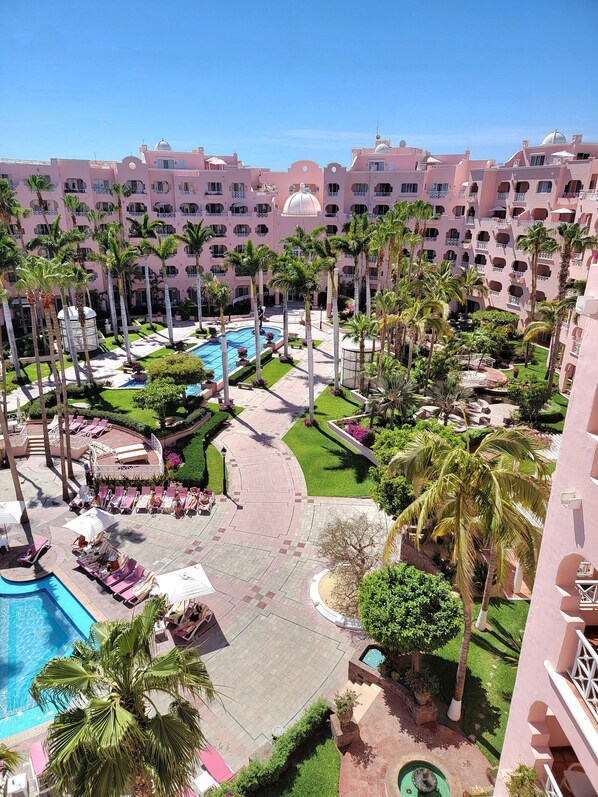 A resort with multiple swimming pools, palm trees, and a large building with balconies.