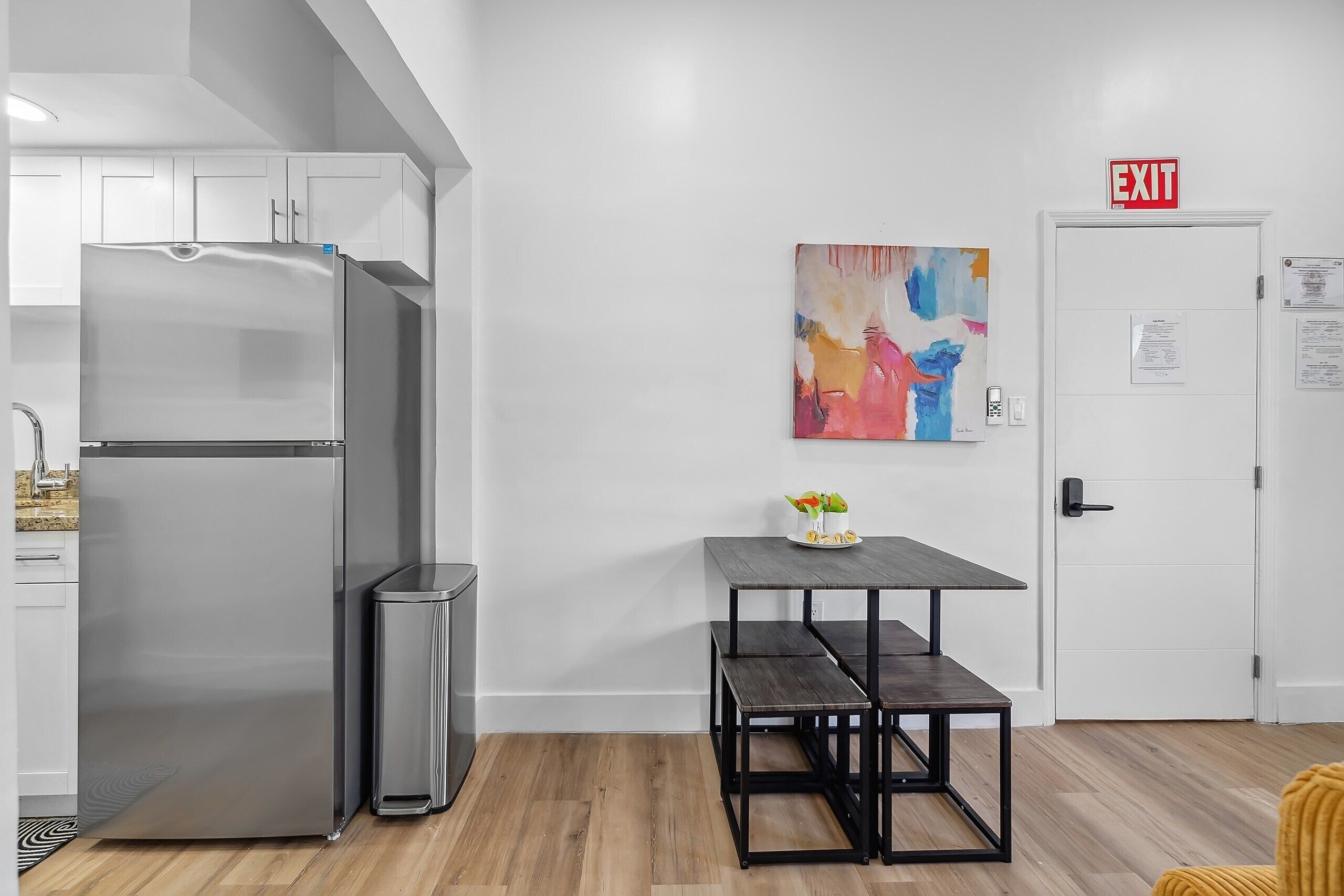A modern kitchen with a stainless steel refrigerator, a trash bin, and a wooden table with benches.