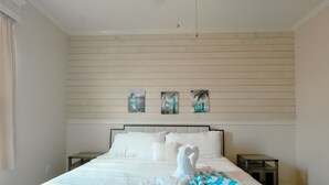 A neatly made bed with white linens and a blue and white checkered blanket. There are three paintings on the wall above the bed, depicting coastal scenes. - Beautiful Resort Near Theme Parks (Kissimmee)