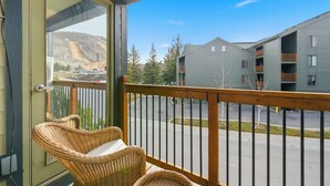 Un balcon avec des fauteuils en osier, une vue sur un immeuble à plusieurs étages et un ciel dégagé.