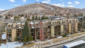 Un immeuble résidentiel à plusieurs étages, doté d’un mélange de balcons et de fenêtres, situé dans une zone vallonnée où la neige recouvre le sol.