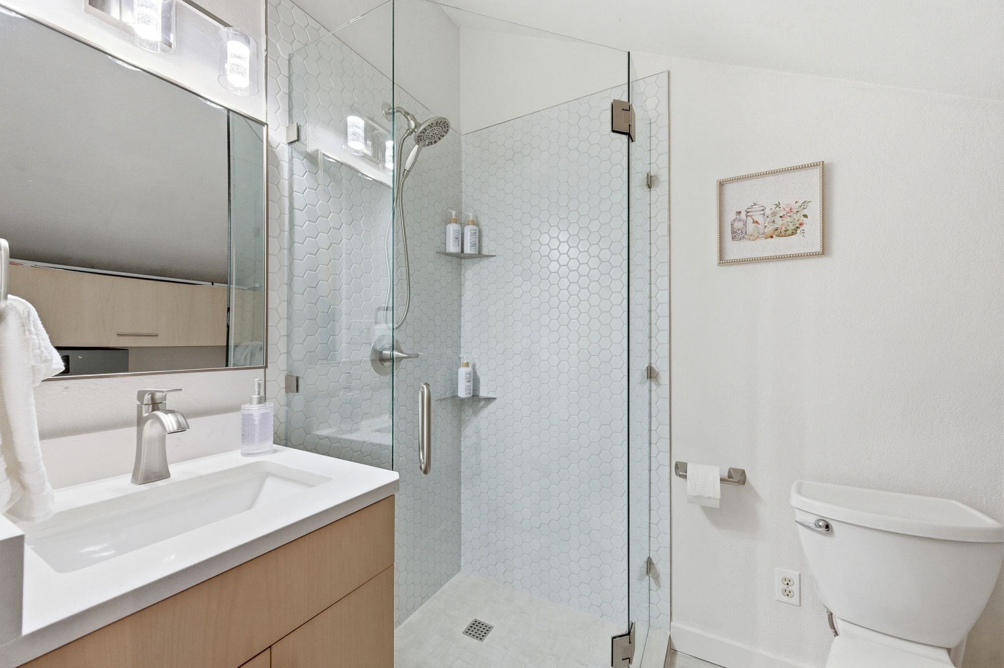 Un baño moderno con ducha de vidrio, un lavamanos blanco y un inodoro.