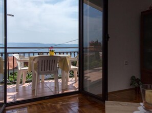 A balcony with a table and chairs, a potted plant, and a view of the sea and mountains. - Apartments Marko (Novi Vinodolski)