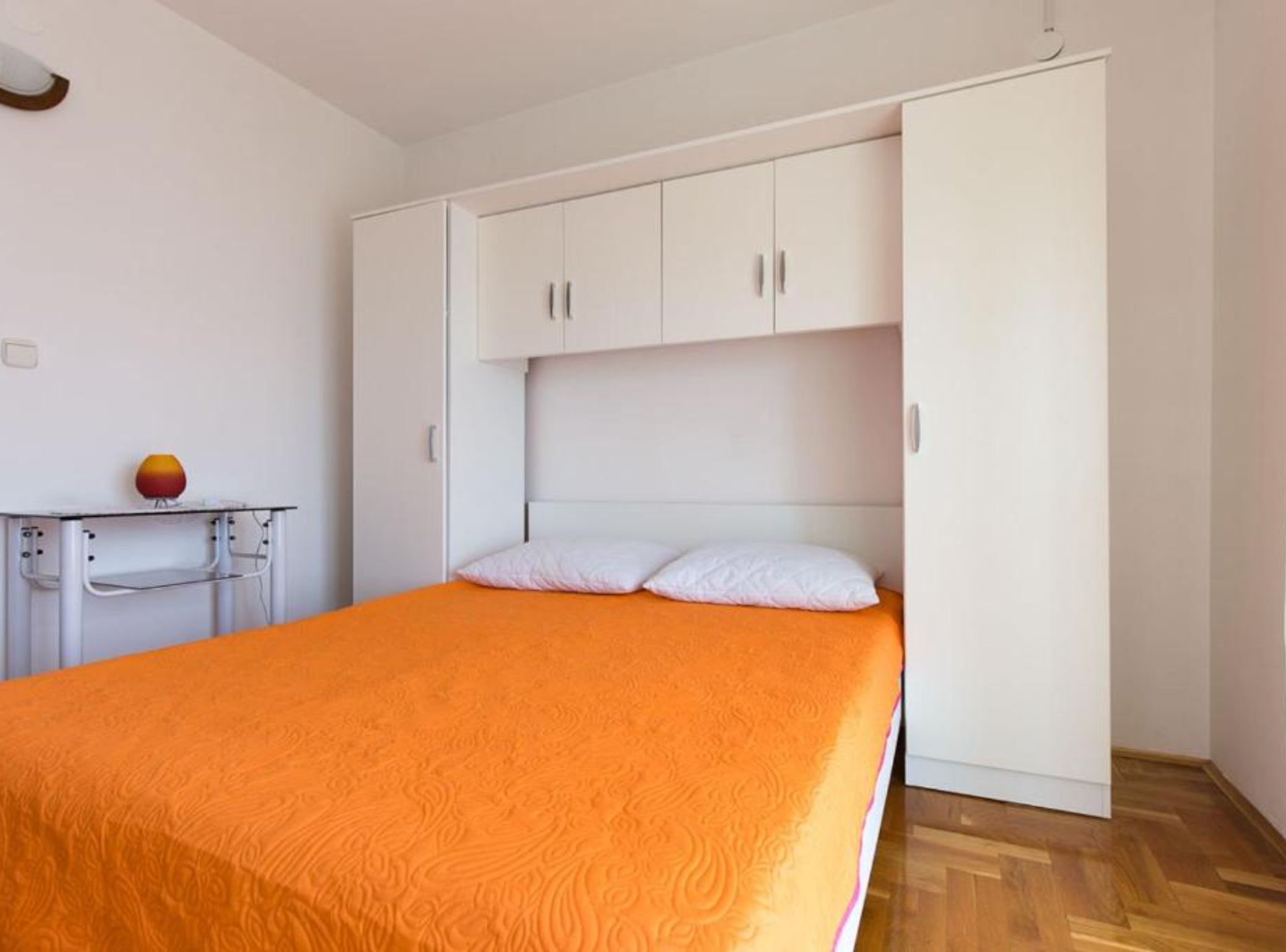 A bedroom with a bed, white wardrobe, and a small table with a lamp.